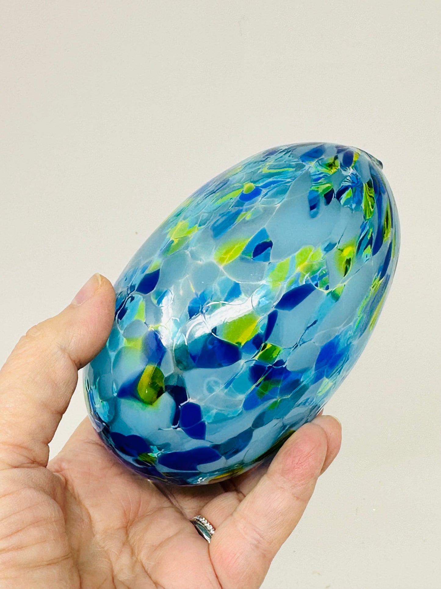 A close-up of a multicolored blue Chuppah glass resting in a hand, designed for the glass-breaking ritual at a Jewish wedding.