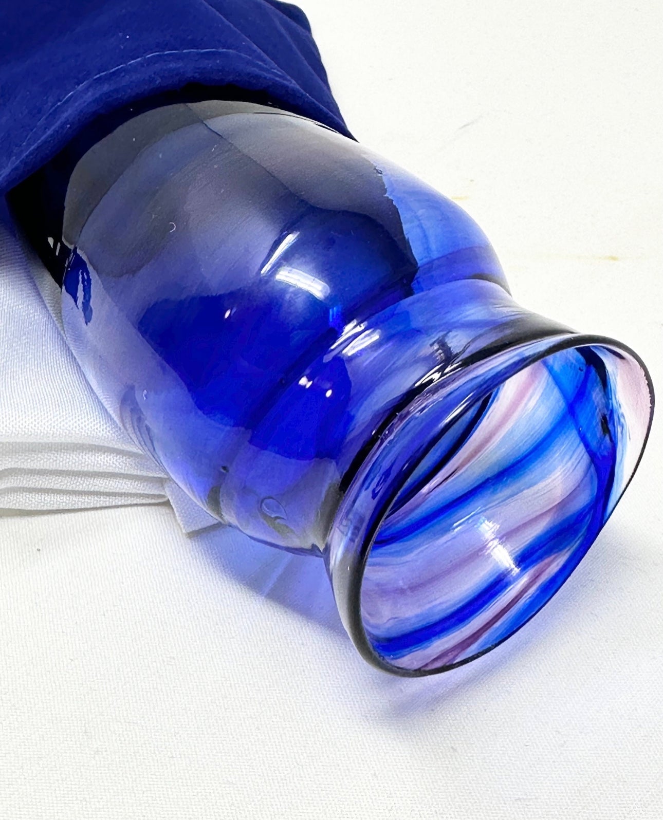 A Chuppah glass in rich purple and cobalt blue tones, placed near a blue velvet pouch partially visible, ready for the glass-breaking ritual at a Jewish wedding.