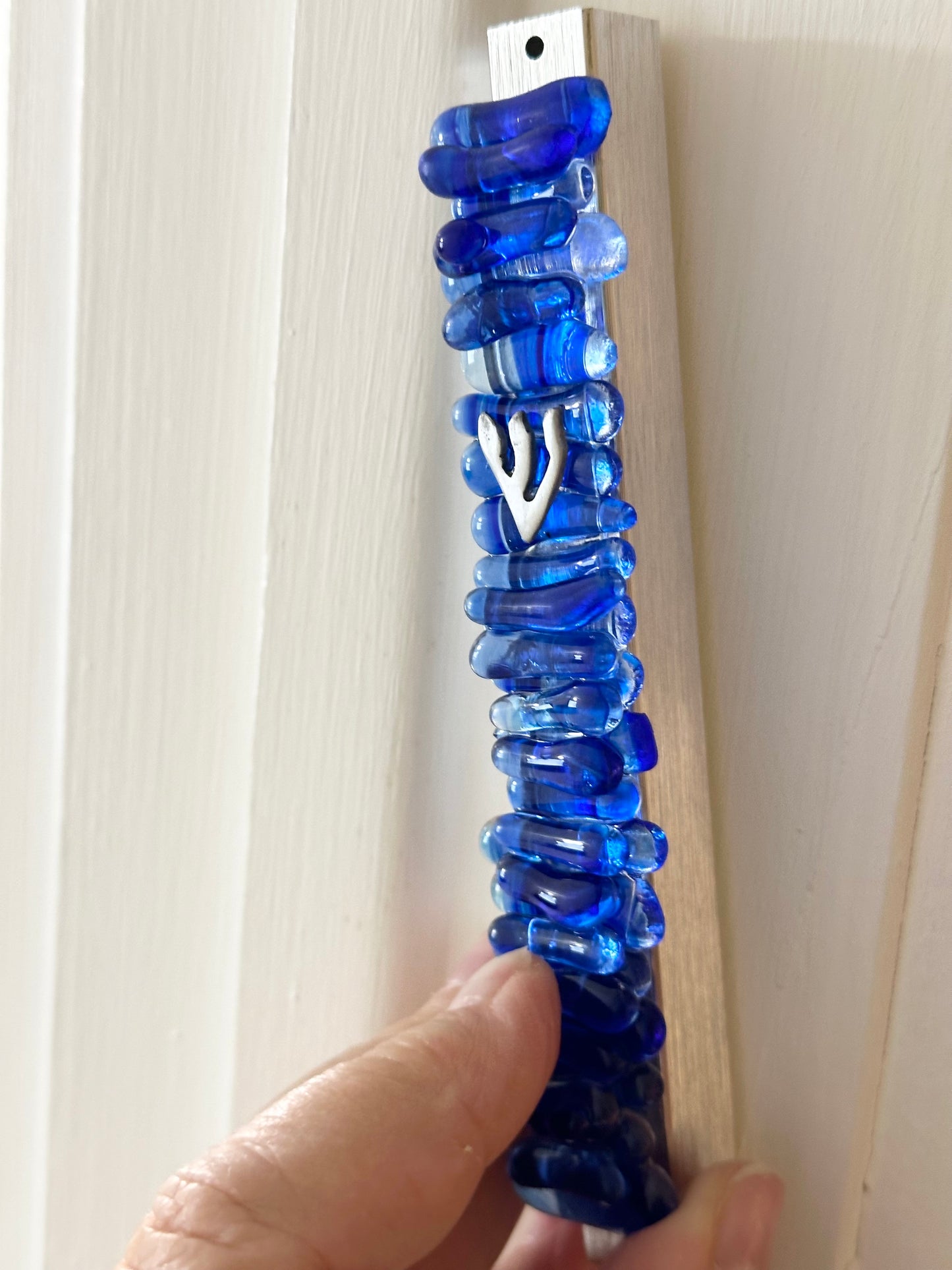  finished mezuzah in cobalt blue being affixed to a doorpost by hand, showcasing its elegant design and ceremonial placement.