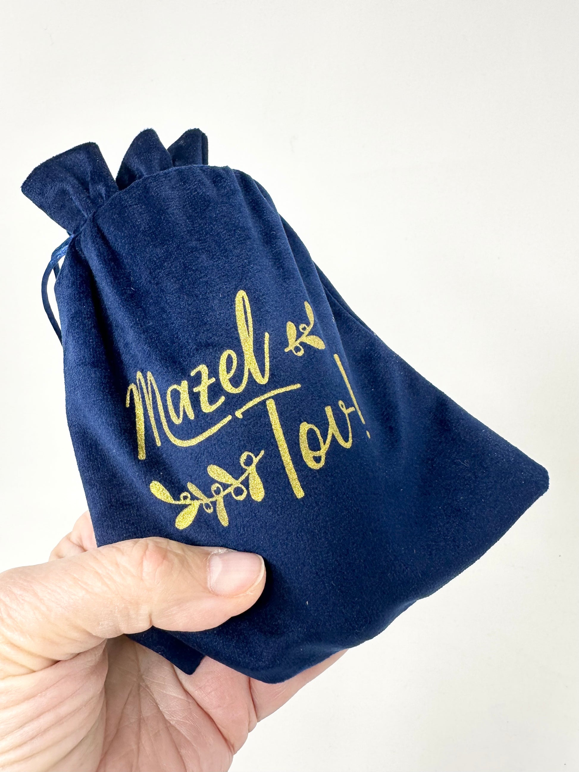 A blue velvet pouch with 'Mazel Tov!' printed in gold, symbolizing celebration and tradition for a Jewish wedding.