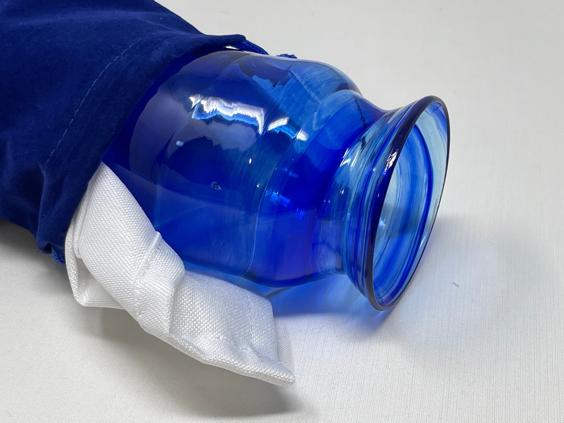 A Chuppah glass in rich cobalt blue tones, placed near a blue velvet pouch and white cloth  partially visible, ready for the glass-breaking ritual at a Jewish wedding.