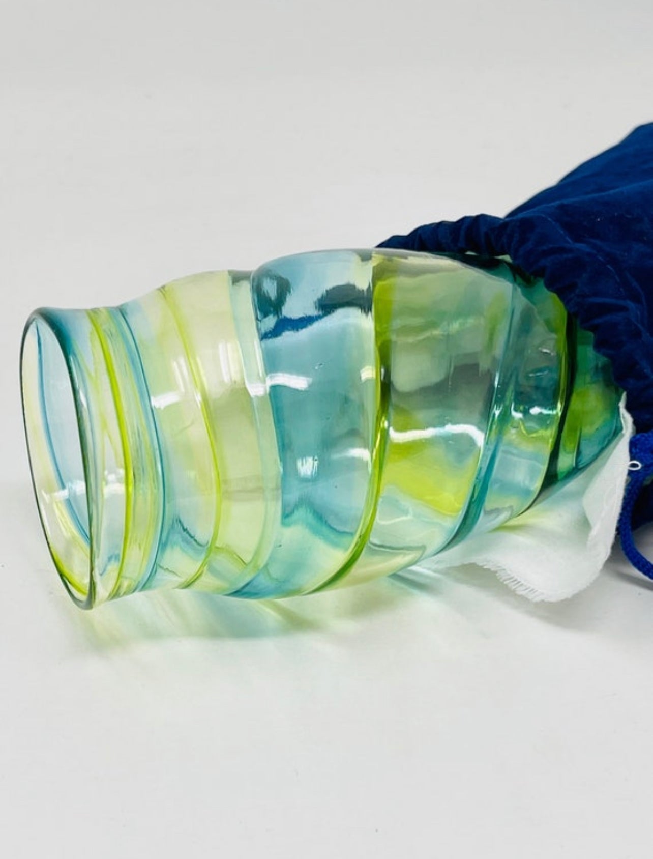 A Chuppah glass in green and yellow tones, placed near a blue velvet pouch partially visible, ready for the glass-breaking ritual at a Jewish wedding."